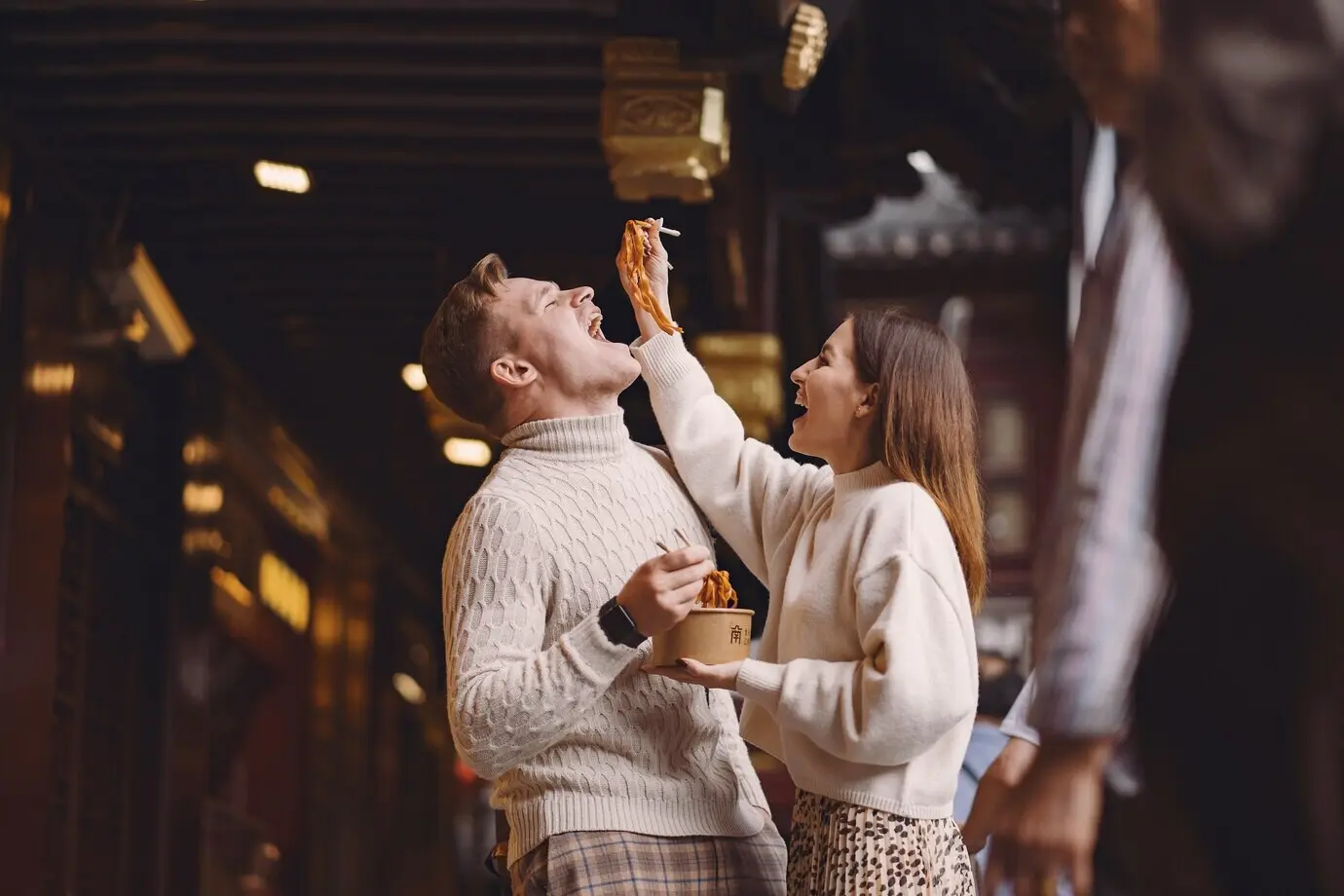 Frisch verheiratetes Paar isst in Shanghai vor einem Lebensmittelmarkt Nudeln mit Essstäbchen.
